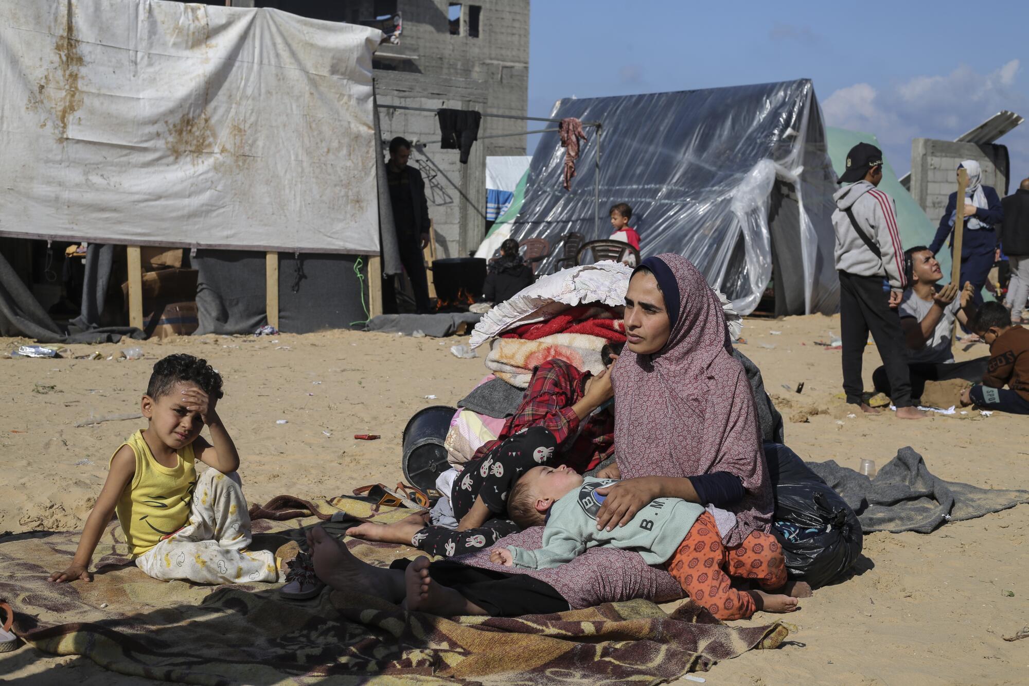 A woman sits outside with children at a tent camp in Gaza