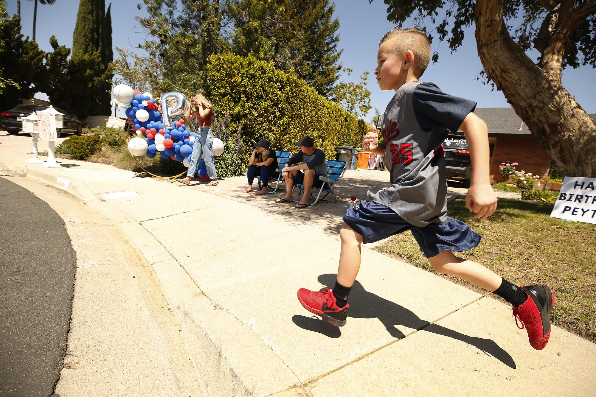 Filled with excitement, Peyton runs by parents Jill and Daniel Buss as fellow teammates from his 2019 Conejo Valley Little League All Star Baseball Team begin to drive by his home in Thousand Oaks to celebrate his 8th birthday.