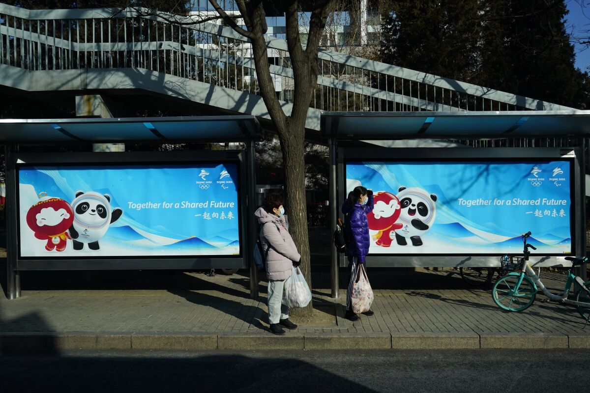 People wait at a bus stop at the 2022 Winter Olympics, Monday, Jan. 31, 2022, in Beijing. (AP Photo/Matt Slocum)