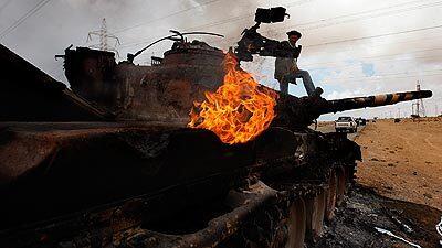 A Libyan rebel celebrates atop a smoldering tank belonging to Moammar Kadafi's forces in Zuwaytina, a vilage east of Ajdabiya, where Kadafi loyalists temporarily halted their retreat.