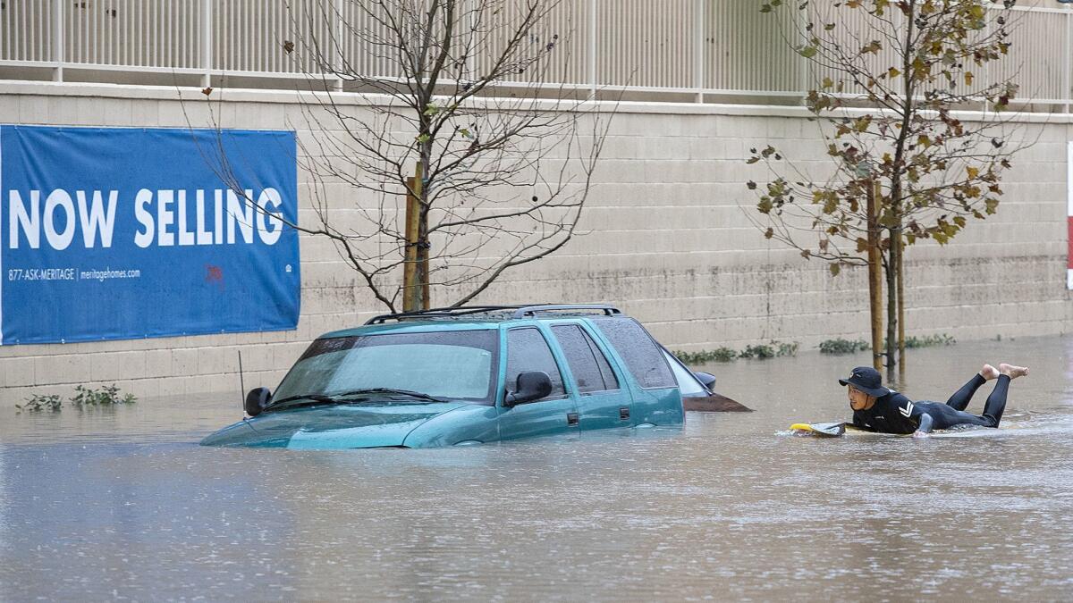 Joe Suzuki paddles past cars submerged in floodwater on Pomona Avenue near 17th Street in Costa Mesa during Thursday’s heavy rain.