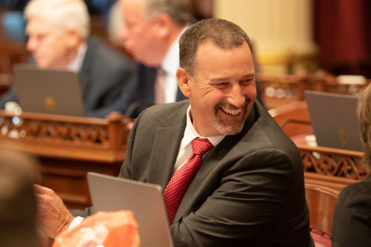 A man at a suit sits in a legislative chamber
