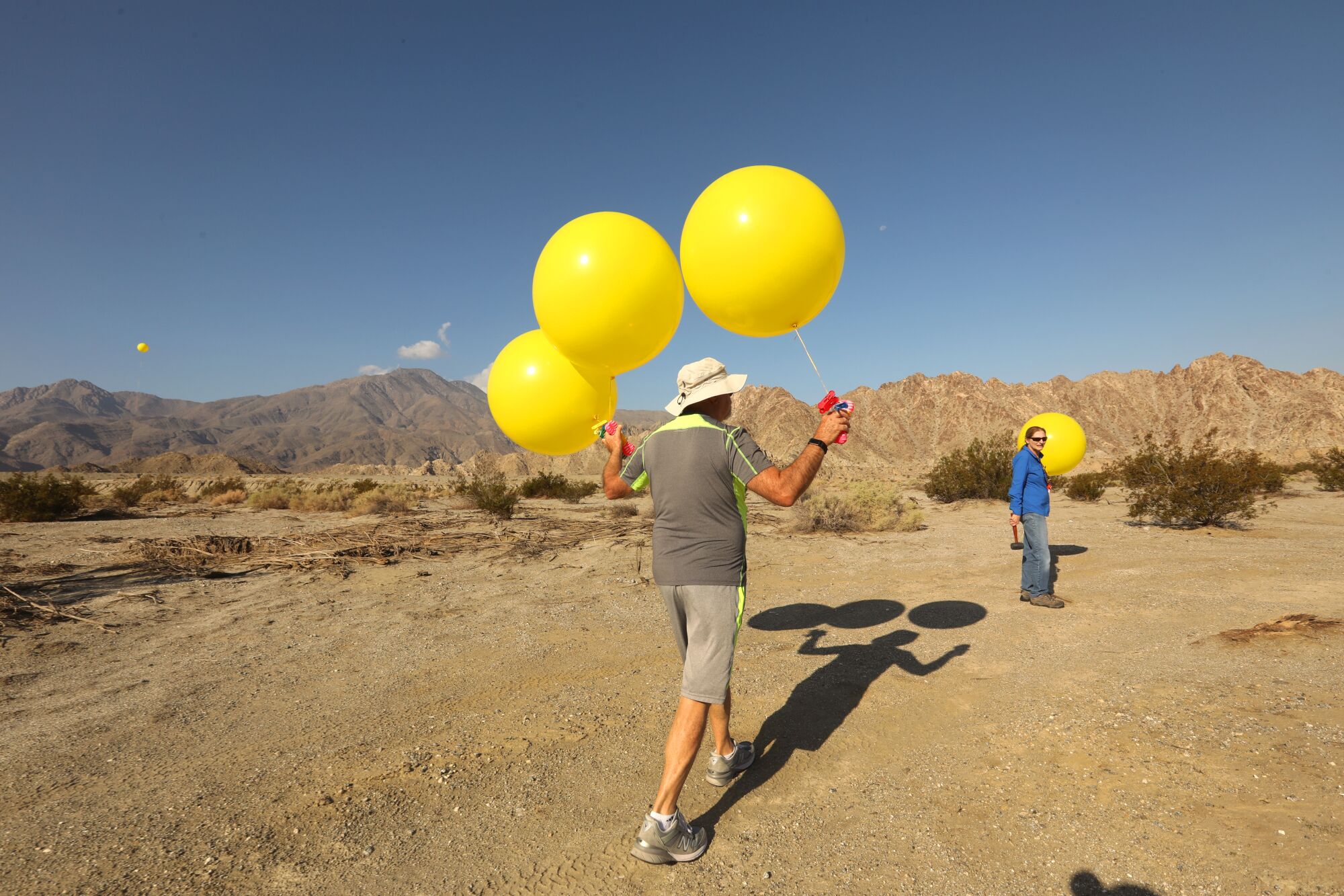 People place yellow balloons in the desert.