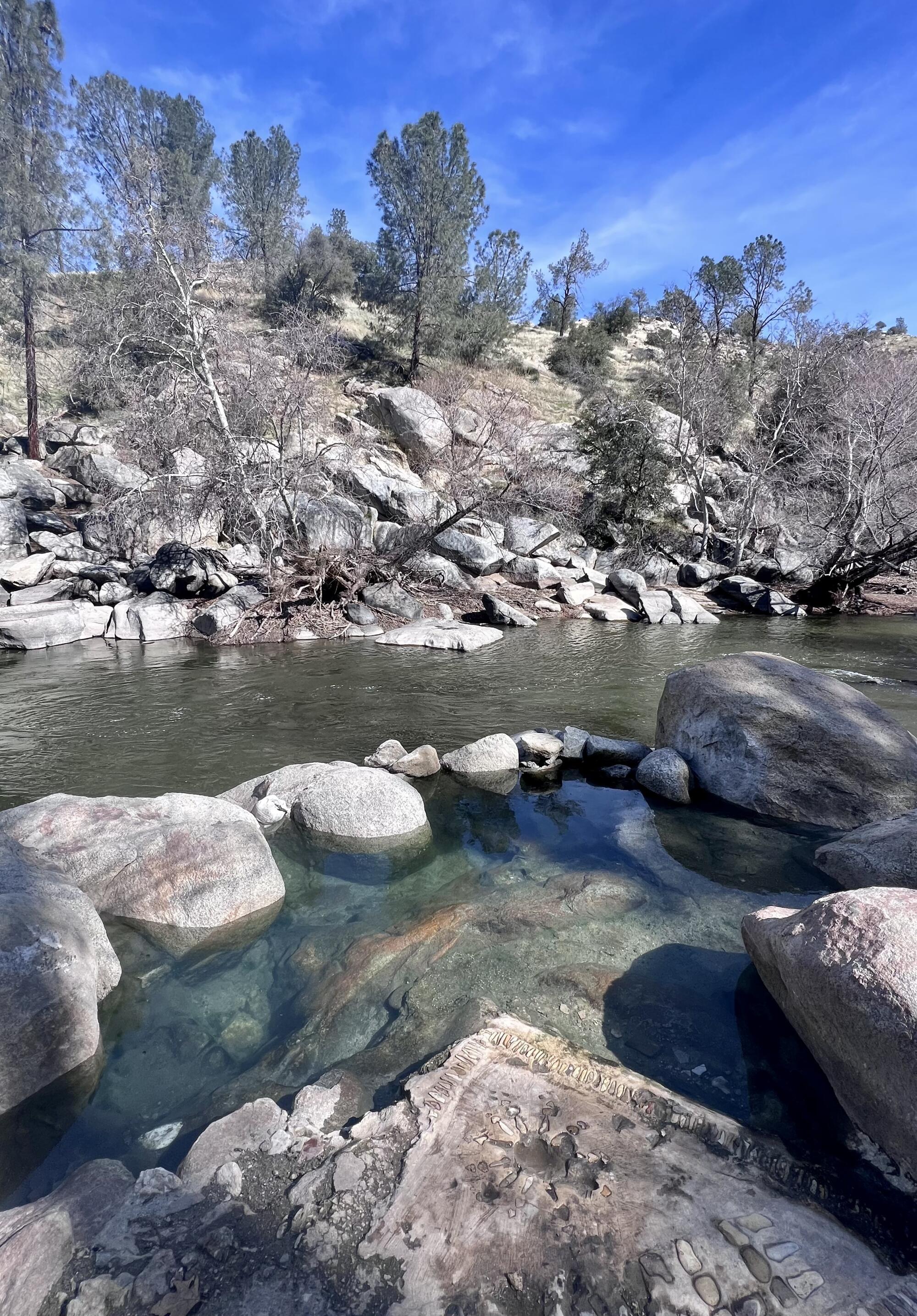 A river flows past a clear rock pool surrounded by rocks and boulders. 