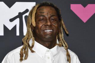 Lil Wayne in a white button down shirt smiling and posing in front of a black backdrop