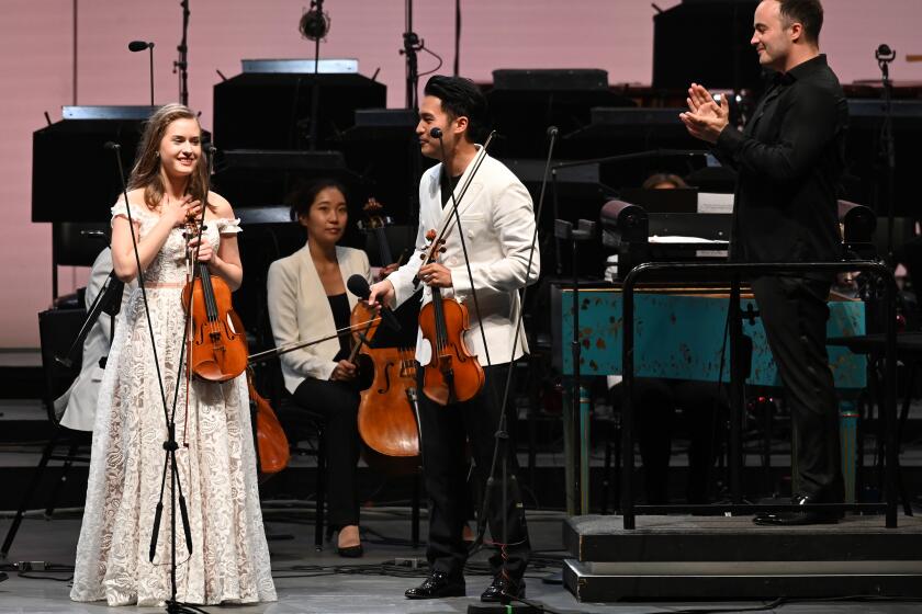 LOS ANGELES, CA -- AUGUST 08, 2019: Laura Kukkonen, 17, of Helsinki, Finland, the winner of the Play with Ray amateur violin contest by the L.A. Philharmonic, takes in the applause after performing BachÕs Concerto for Two Violins with Ray Chen and Ben Gernon (right) conducting. (Myung J. Chun / Los Angeles Times)