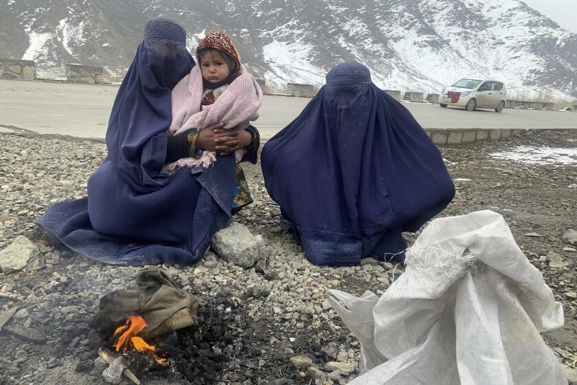 Gulnaz, left, keep her 18-month-old son warm themselves as they wait for alms in the Kabul - Pul-e-Alam highway eastern Afghanistan, Tuesday, Jan. 18, 2022. The Taliban's sweep to power in Afghanistan in August drove billions of dollars in international assistance out of the country and sent an already dirt-poor poor nation, ravaged by war, drought and floods, spiralling toward a humanitarian catastrophe. (AP Photo/Kathy Gannon)