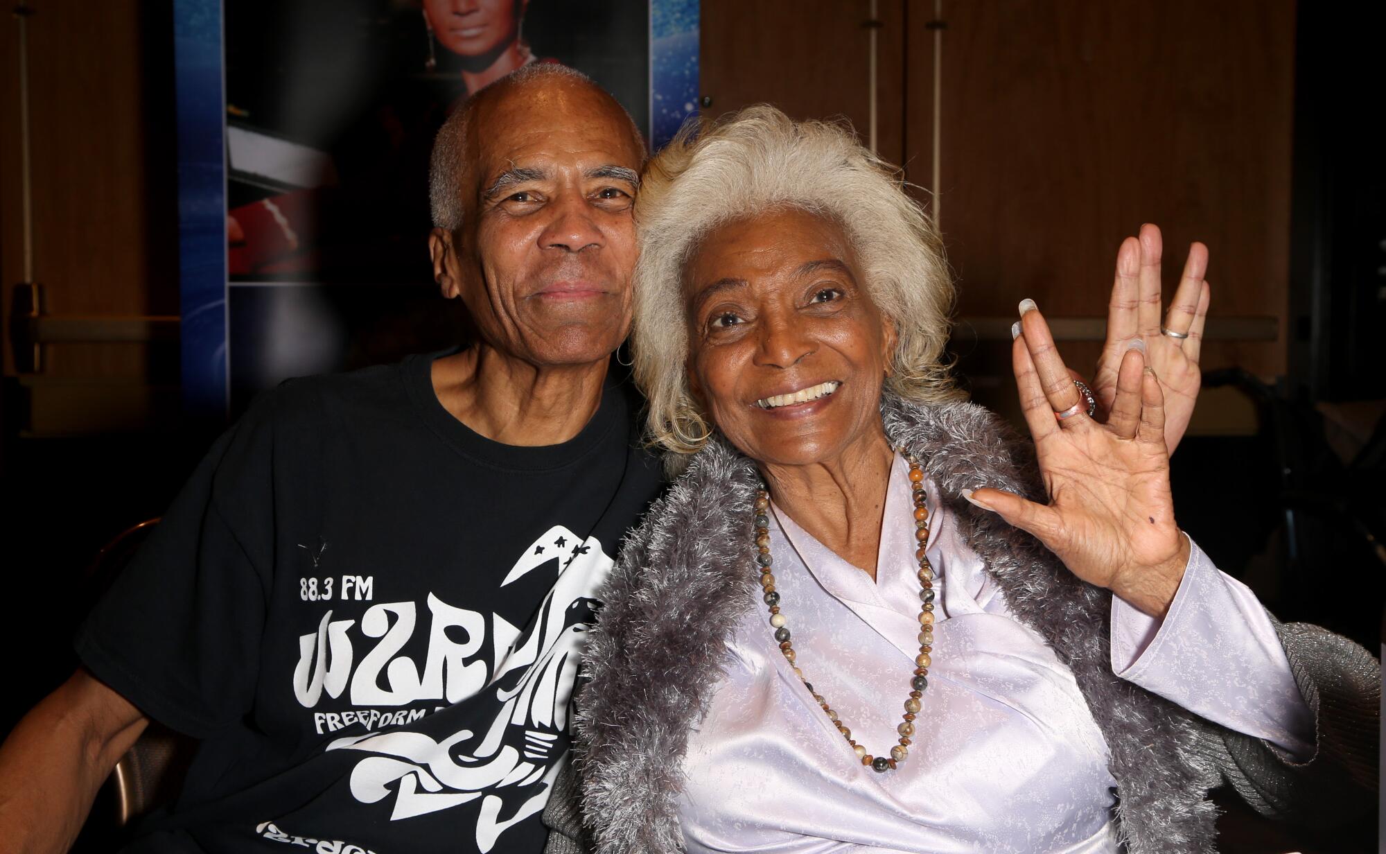 A middle-aged man, left, smiling with his older mother, who is spreading her hand in a "Star Trek" symbol. 