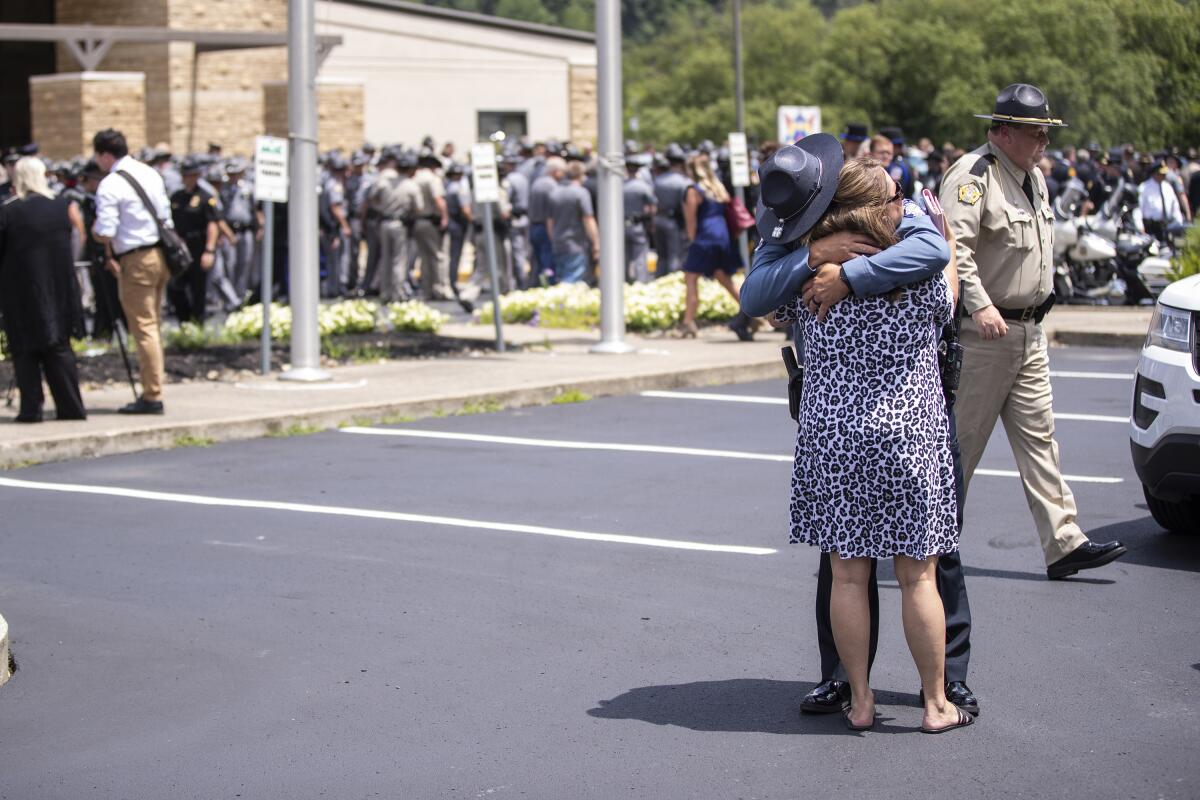 Law enforcement officer embraces a woman in the making lot after the funeral service for Floyd County Deputy William Petry at the Mountain Arts Center in Prestonsburg, Ky., Tuesday, July 5, 2022. Petry and two Prestonsburg city police officers were killed while serving a warrant at a home in the county. (Silas Walker/Lexington Herald-Leader via AP)