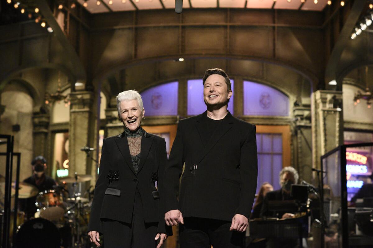 A woman and a man in matching black outfits smile onstage.