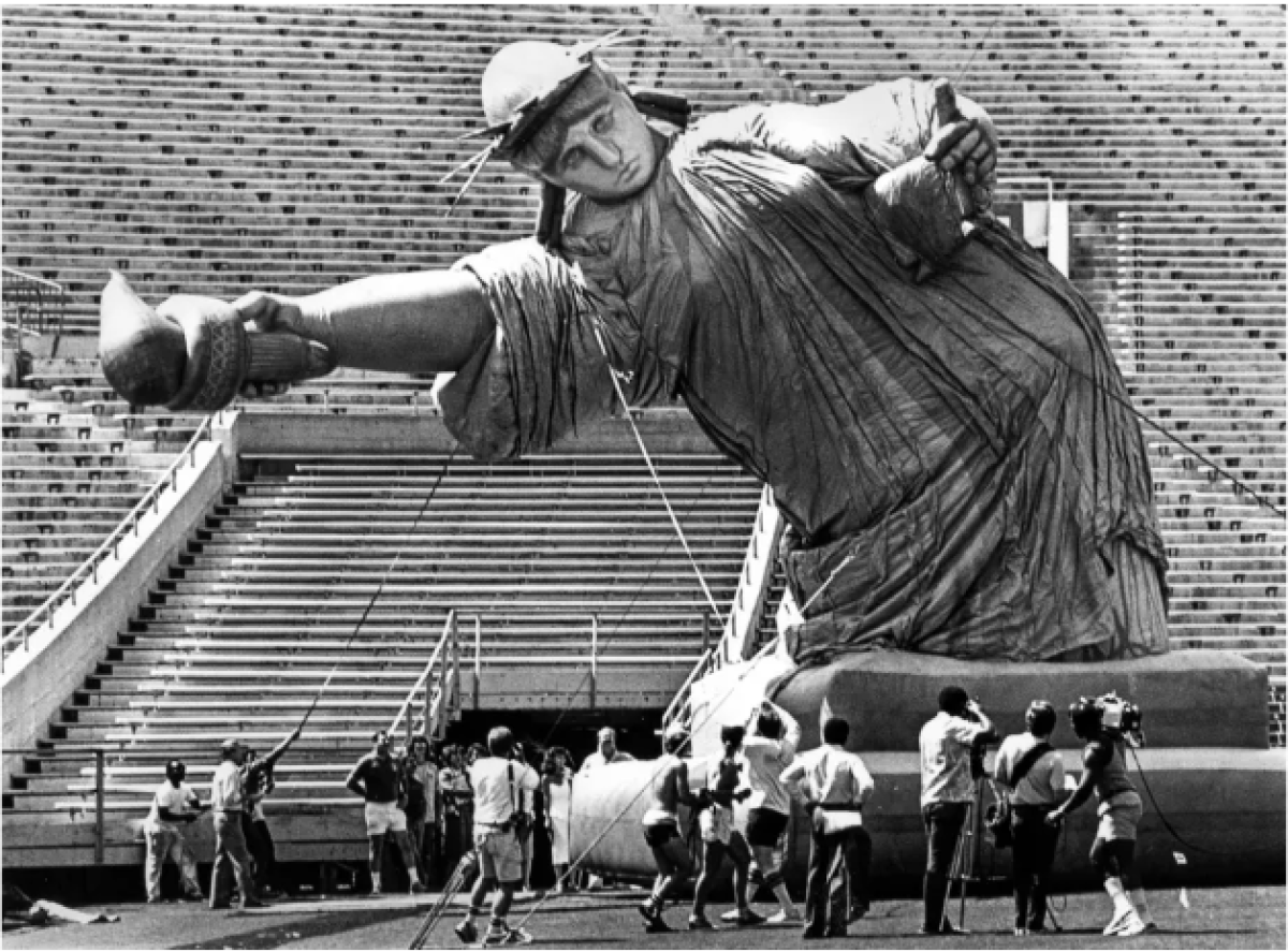 A 50-foot Statue of Liberty balloon begins to take shape as people stand around it in a stadium