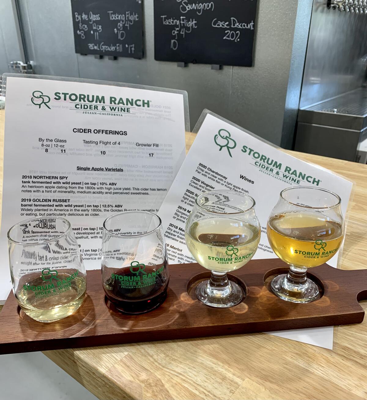 A tasting flight of four beverages sitting on a wooden table with a menu
