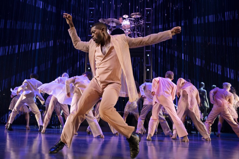 A man does the twist with a bunch of dancers is the background, facing away