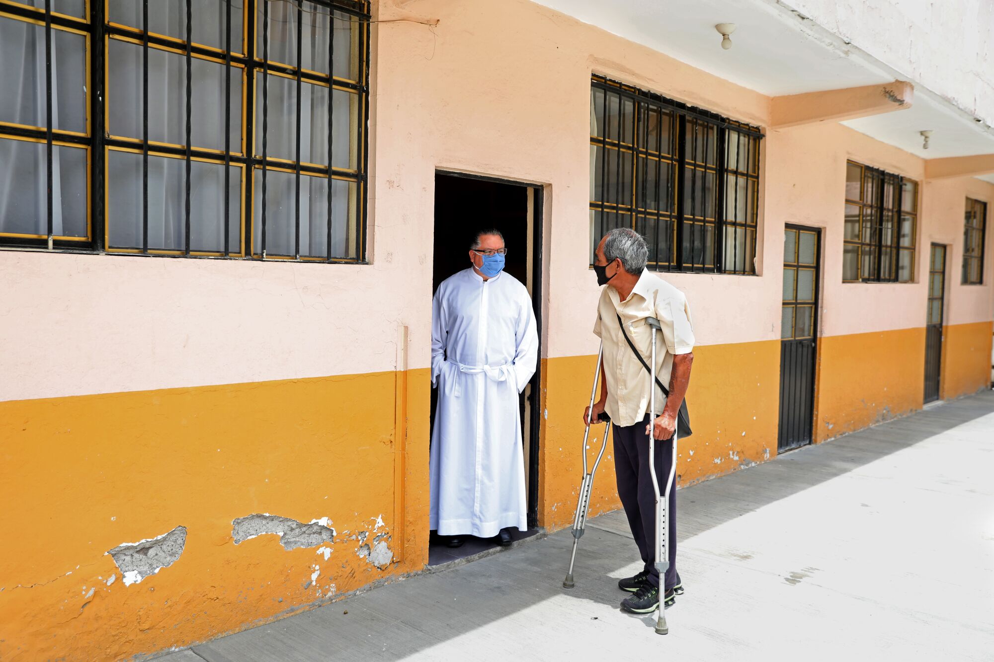 A man on crutches talks to a priest in white robes