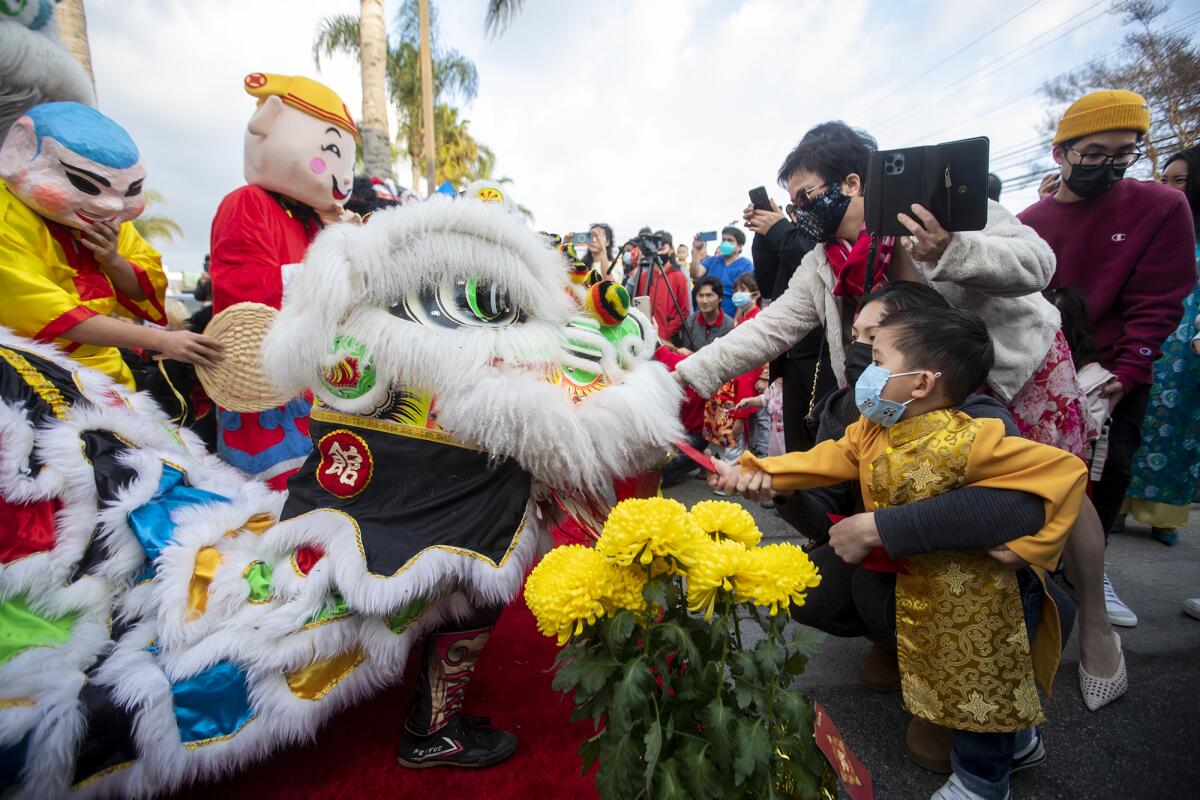 Two children feed an envelope to a member of the Qing Wei Lion and Dragon Cultural Troupe.
