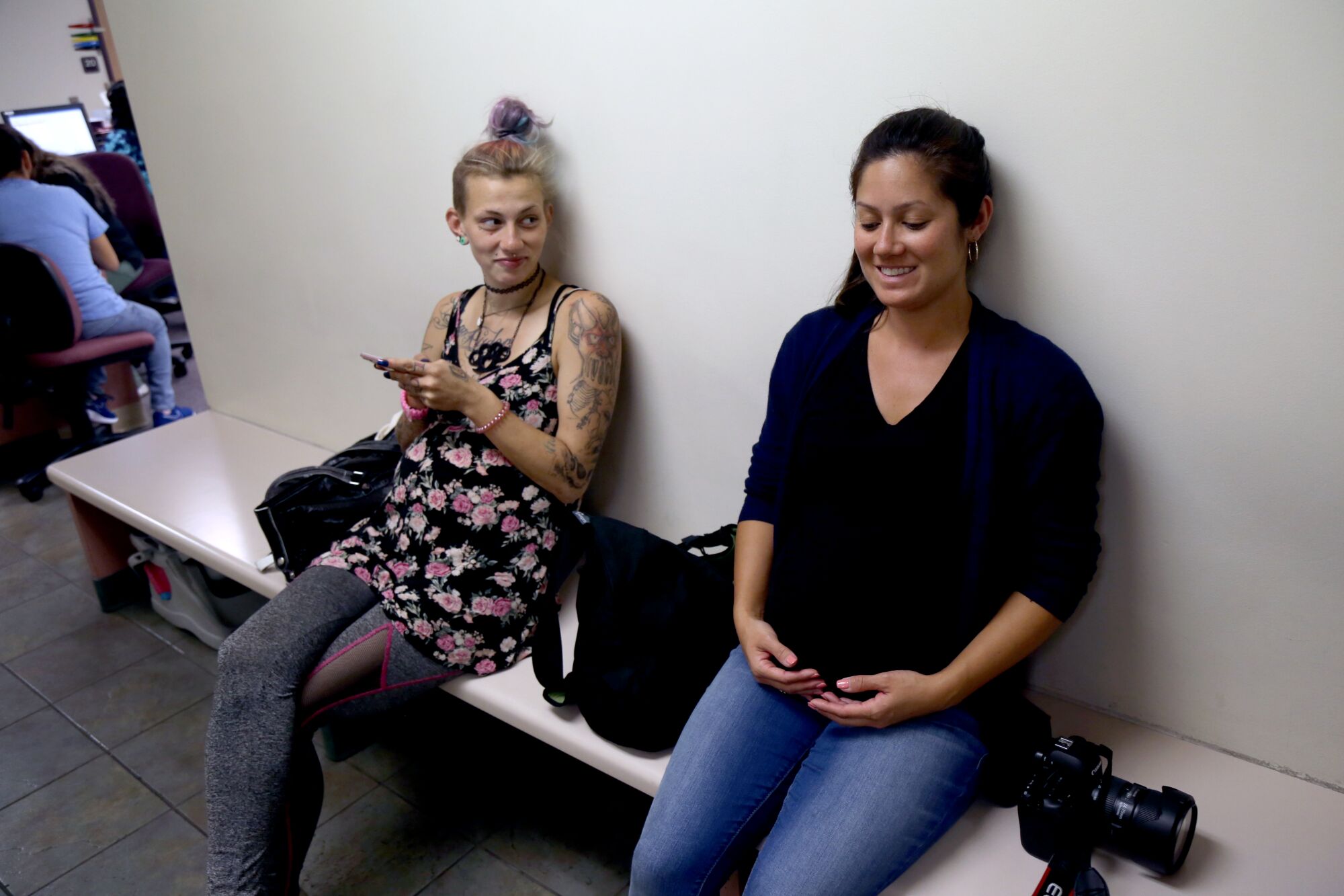 Two pregnant women sit on a bench with one woman looking at the other.