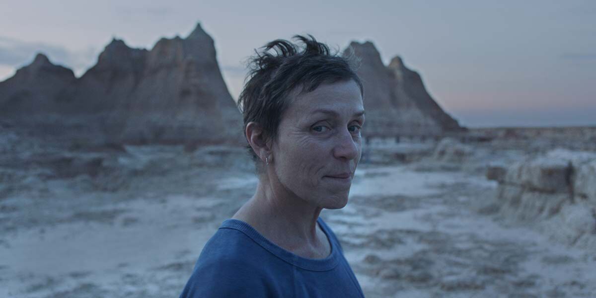 A woman with short, spiky hair stands in the desert at dusk.