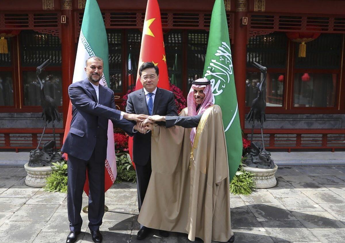 Iranian and Saudi Arabian foreign ministers shaking hands while their Chinese counterpart looks on