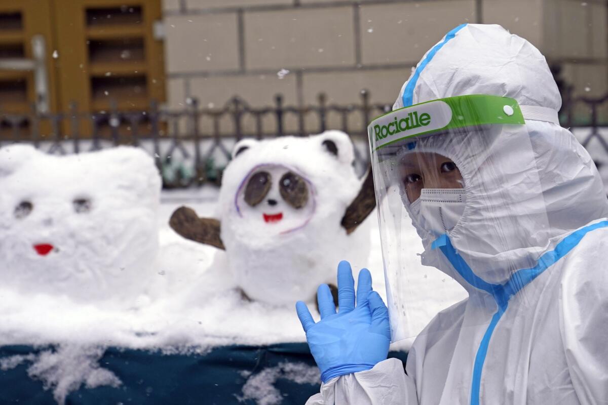 A worker in protective gear waves next to snowmen shaped like the Olympics mascot