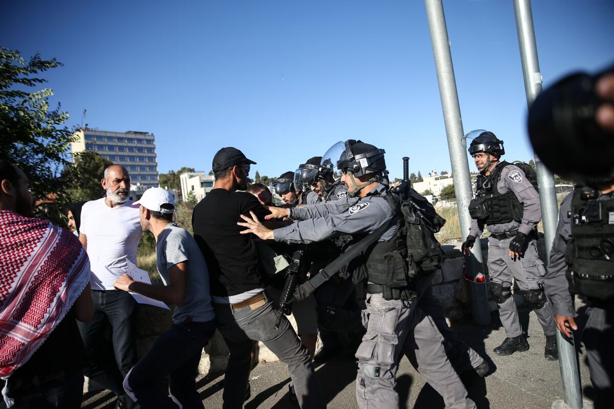 A uniformed man in protective gear pushes a civilian man.