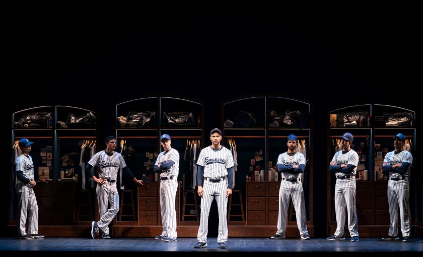 The cast of "Take Me Out" stands in baseball uniforms on a stage set made to look like a locker room.