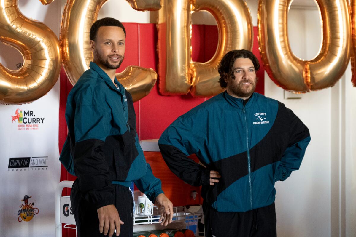 Stephen Curry and Adam Pally in green and black warmup suits.