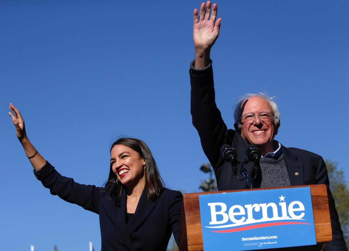 Rep. Alexandria Ocasio-Cortez (D-N.Y.) and Sen. Bernie Sanders (D-Vt.) wave at the crowd.