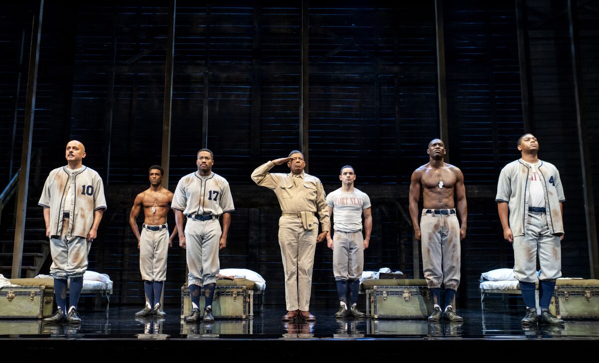 Soldiers stand at attention in various stages of dress in a barracks onstage