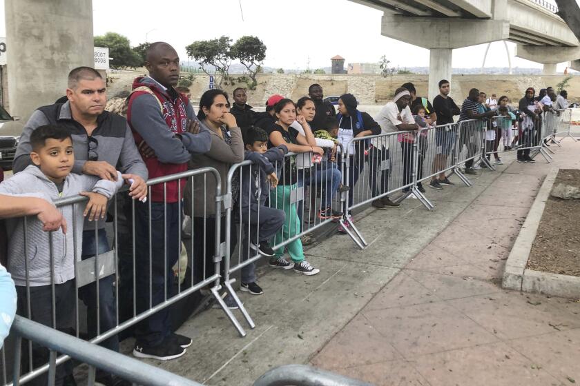 ARCHIVO - En esta fotografía de archivo del 26 de septiembre de 2019, solicitantes de asilo en Tijuana, Mexico, escuchan nombres que están siendo anunciados a partir de una lista de espera para solicitar asilo en un cruce fronterizo en San Diego. (AP Foto/Elliot Spagat, archivo)