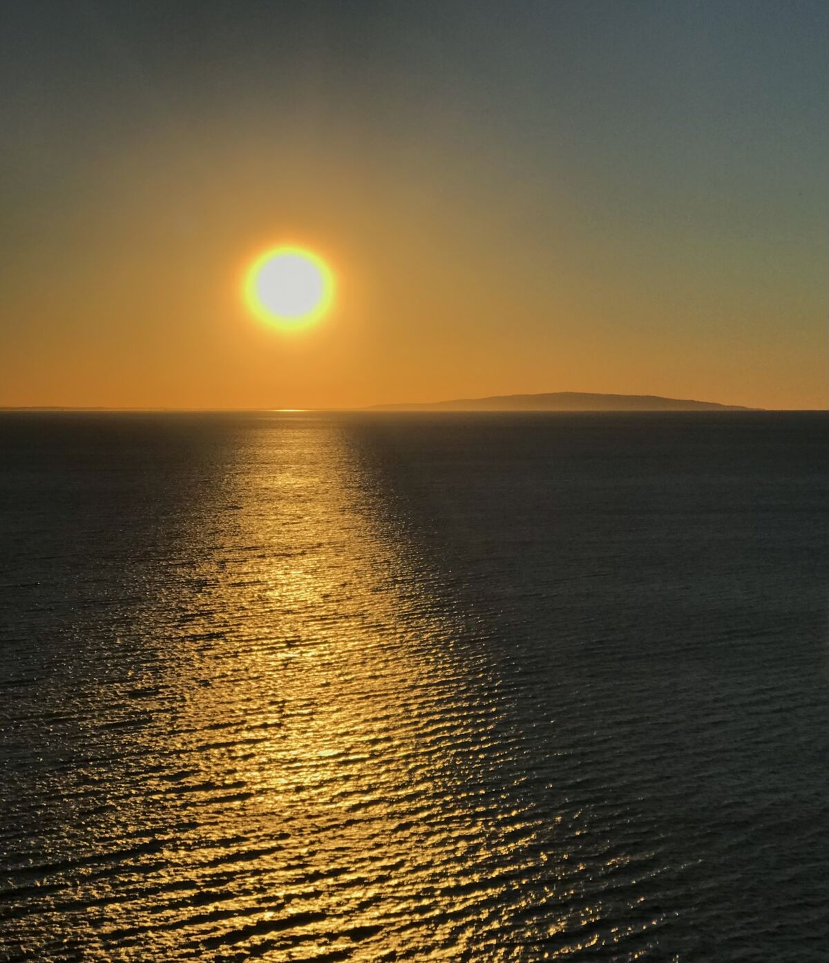 The view from the top of Point Dume shows the sun shining over the Pacific with the Los Angeles shoreline in the distance.