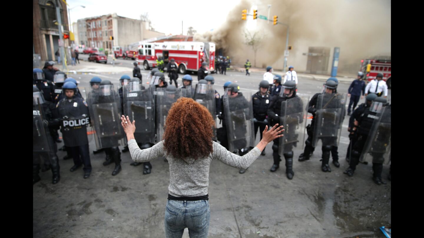 A woman faces down a line of Baltimore police officers in riot gear.