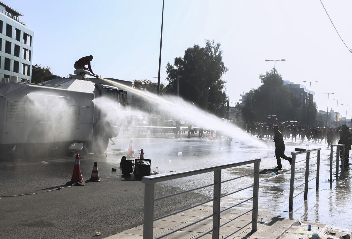 Police fire water cannon at protesting firefighters gathered outside Greece's Climate Change and Civil Protection Ministry in Athens on Friday, Nov. 5, 2021. The protesters are calling on the government to extend their contracts in the wake of massive wildfires in southern Greece in August, arguing that more firefighters are needed to combat the effects of climate change.(Giannis Dimitropoulos /InTime News via AP)