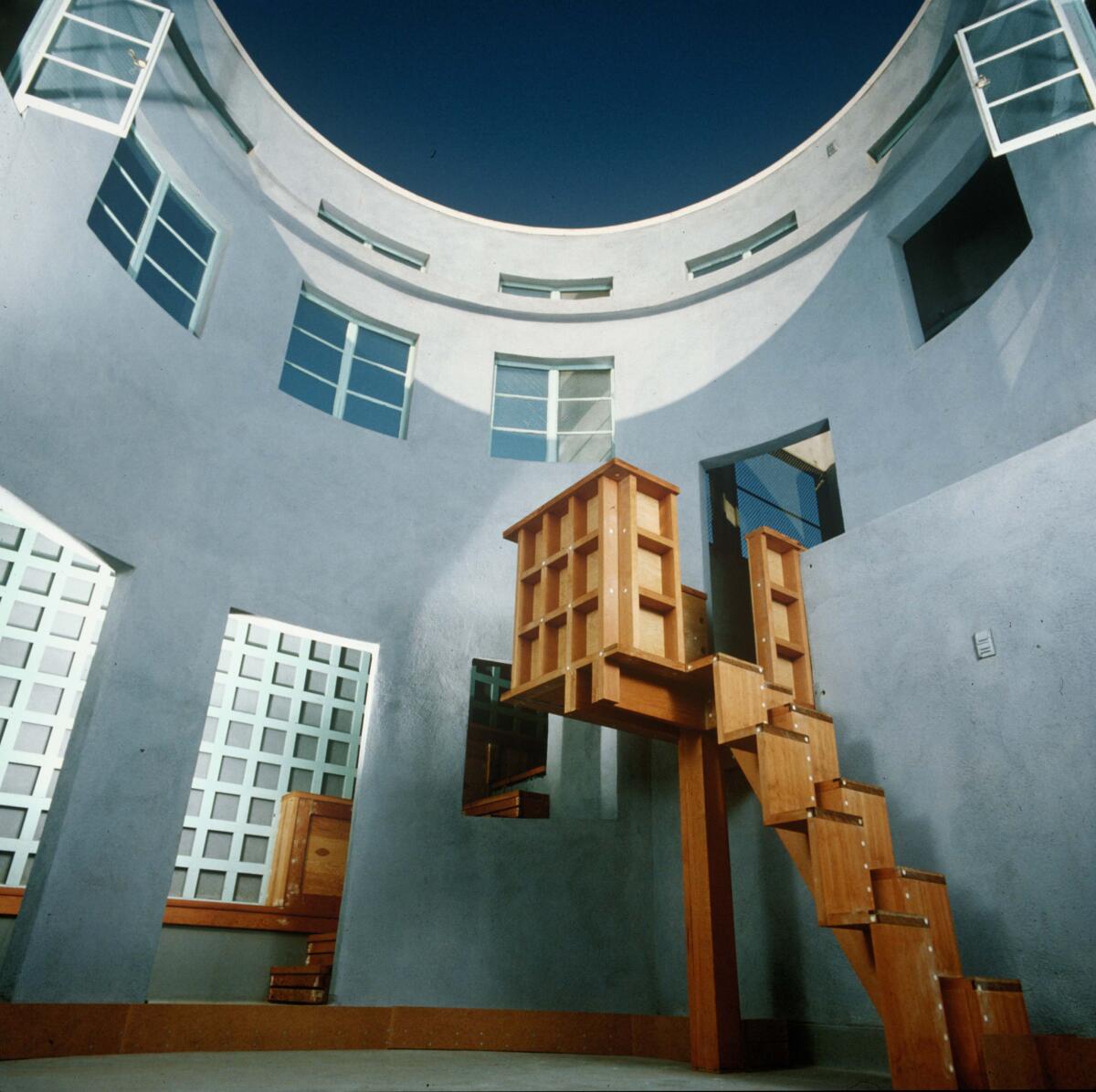 An upward view shows a rounded, Postmodern two-story courtyard painted blue with jagged wooden stairs