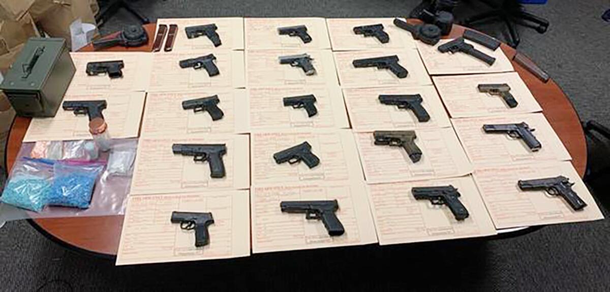 Individual guns each rest atop a yellow form on a table, along with items including bags containing blue substances 