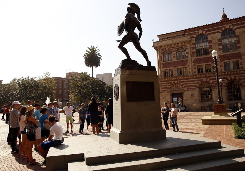 A tour group gathers around the Tommy Trojan statue at the center of USC's University Park campus on a sunny day