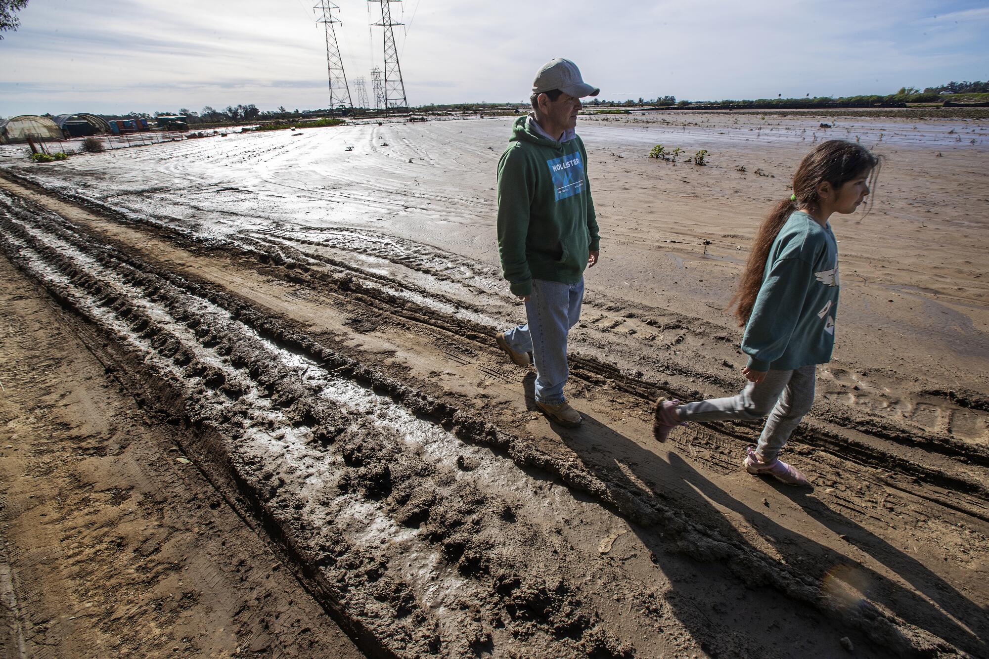 A man and a young girl walk by a muddy field.