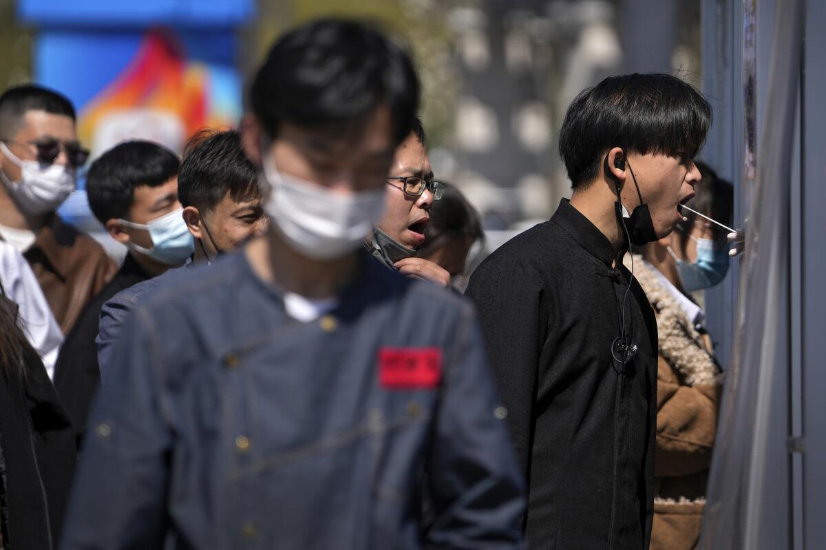 Workers wearing face masks line up to get their throat swab at a coronavirus testing site.