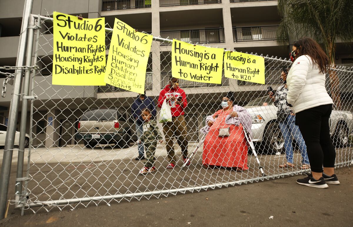 A woman talks to people behind fencing at a motel parking area.
