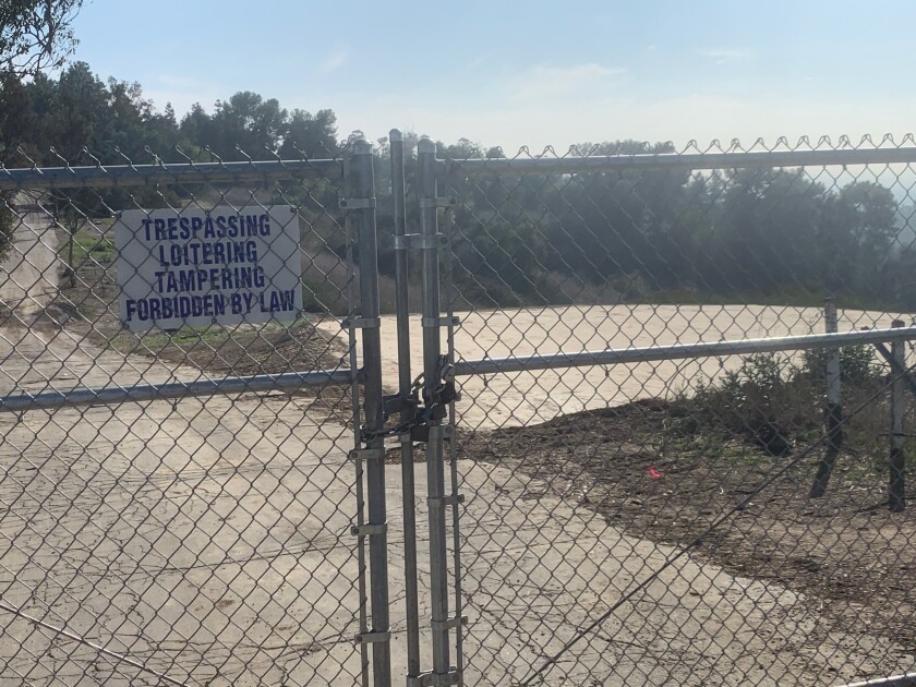 A chain-link fence with a 'no trespassing' sign with empty land behind it