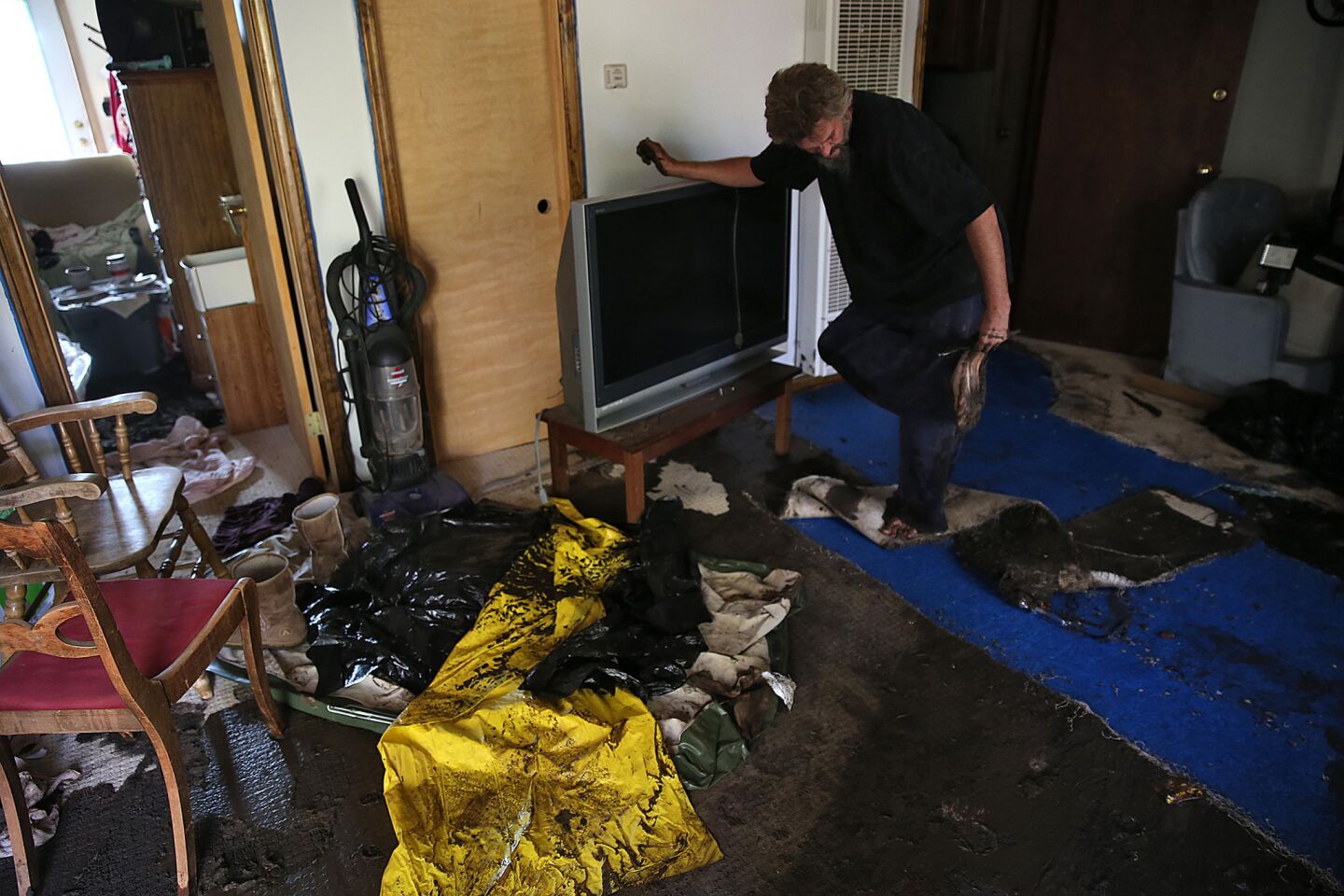 Jason DeBerge, 45, wipes mud from his feet as he tries to remove damaged carpet from his Lake Hughes home.