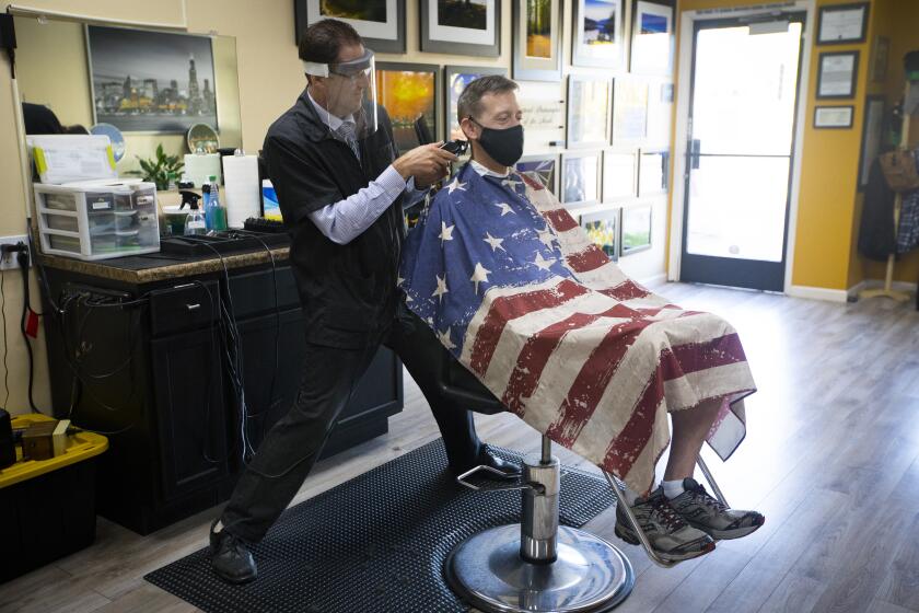 TEMECULA, CA - MAY 26: Gene Kelley, left, co-owner of Skyline Barber Shop cuts Dan Collins, right, hair on Tuesday, May 26, 2020 in Temecula, CA. Gov. Gavin Newsom says California counties that have been granted regional variances allowing more types of businesses to reopen can now permit the reopening of barbershops and hair salons, with modifications such as protective gear and face coverings during the coronavirus pandemic. (Francine Orr / Los Angeles Times)