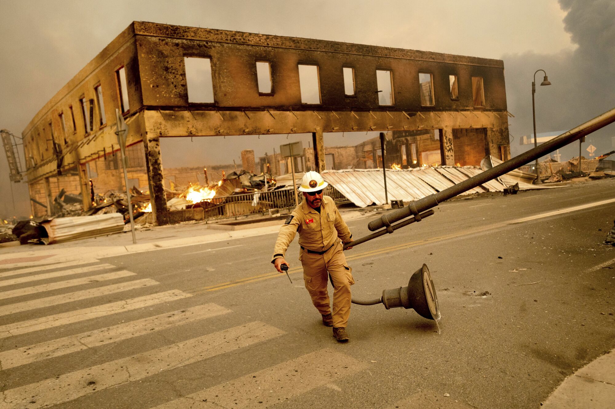 A man drags one end of a light pole across a street in front of a burned-out two-story building