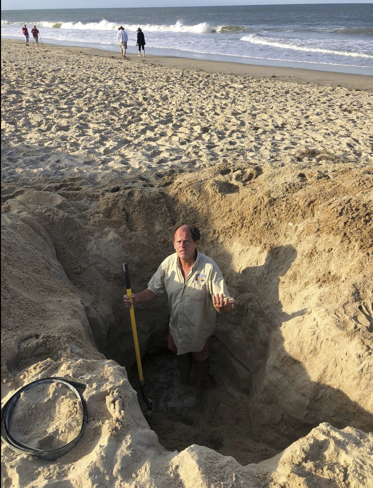 In this image provided by the Town of Kill Devil Hills, N.C., David Elder, ocean rescue supervisor for Kill Devil Hills, N.C, stands in a hole he estimates to be 7 feet deep on Sunday, May 15, 2022. The town on North Carolina’s Outer Banks has issued a plea to beachgoers about the dangers of digging holes on the beach and to cover them up to prevent problems. (Town of Kill Devil Hills via AP)