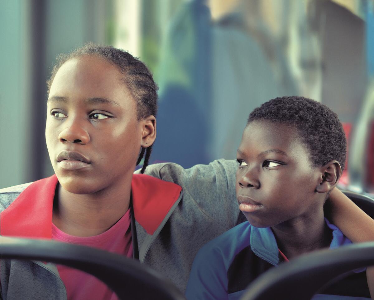 On public transport, a young woman wraps an arm protectively around a boy's shoulders.