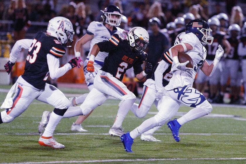 Newport Harbor's Justin Mccoy breaks through the Huntington Beach defense who is giving chase and runs a long way for a touchdown in Sunset League football at Huntington Beach High School on Friday, October 11, 2019.
