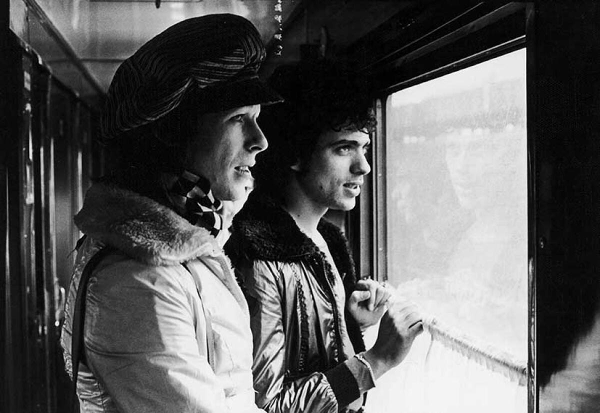 Two men in a railroad car corridor look out a window.