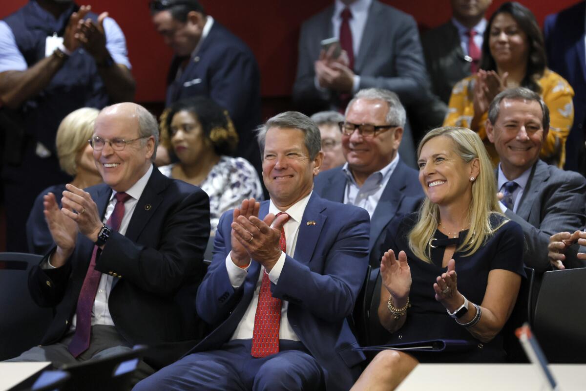 College Football Playoff executive director Bill Hancock, left, Georgia Gov. Brian Kemp and Georgia first lady Marty Kemp applaud during a press conference at Mercedes-Benz Stadium, Tuesday, Aug. 16, 2022, in Atlanta, announcing that the CFP National Championship NCAA college football game will be played at Mercedes-Benz Stadium in 2025. (Jason Getz/Atlanta Journal-Constitution via AP)