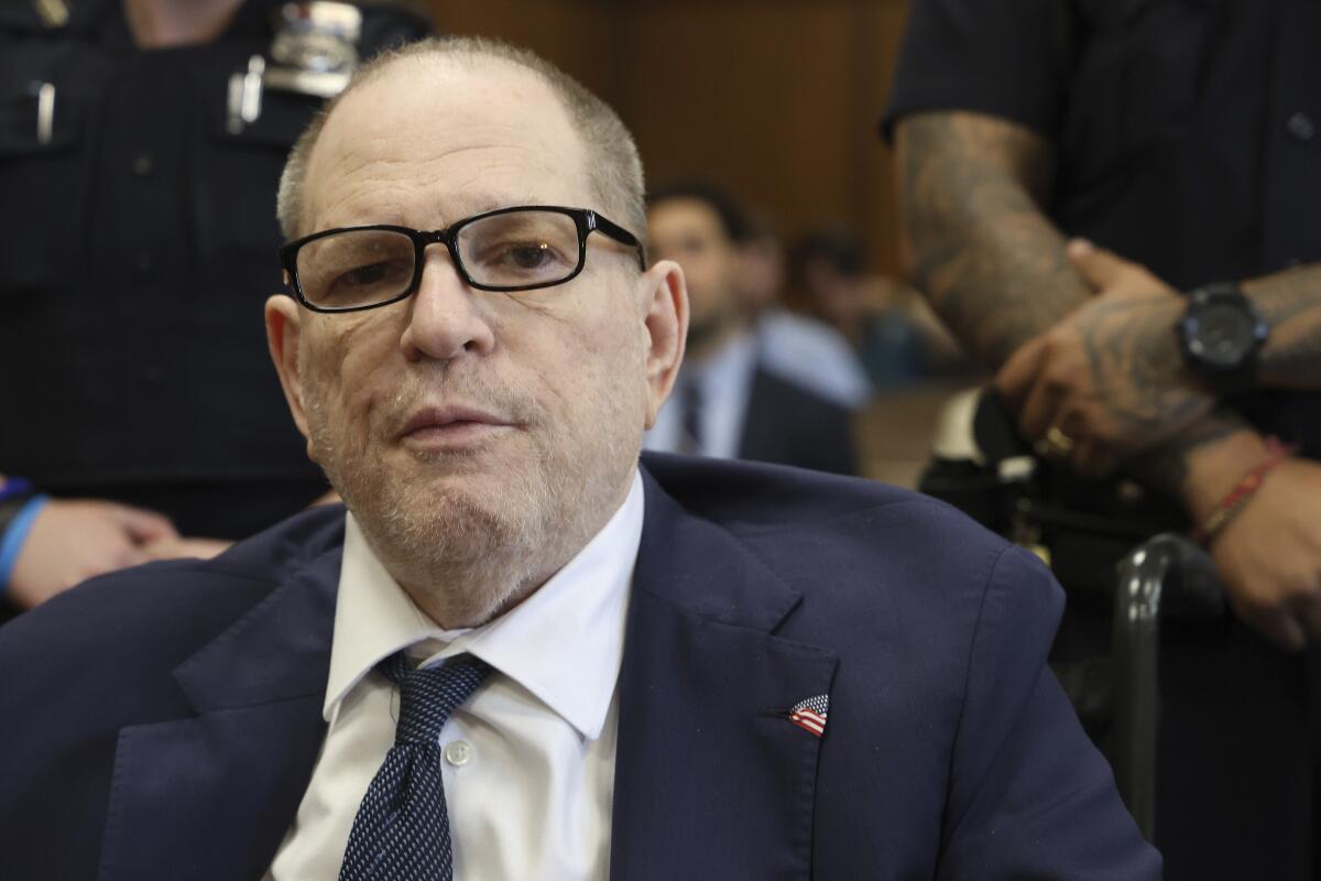 Harvey Weinstein in a suit and glasses sits in a courtroom.
