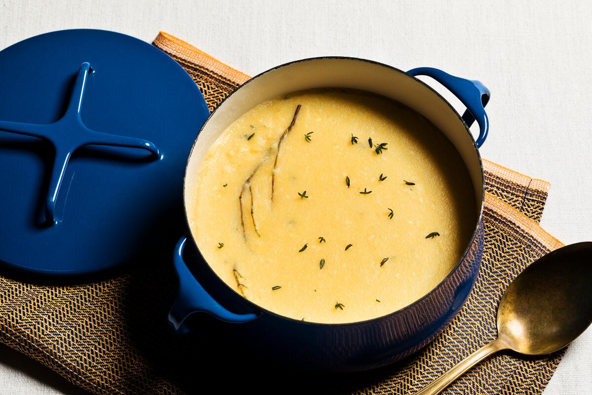 A blue Dutch oven that contains yellow polenta dotted with thyme.