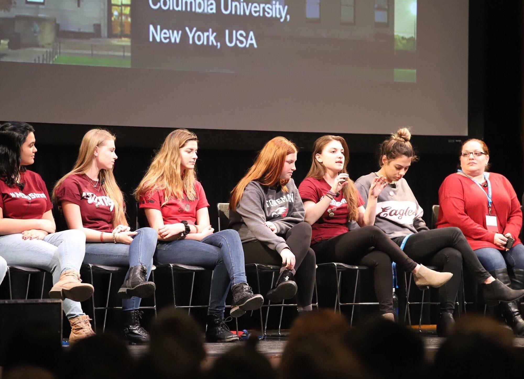 Students sit in a line on a stage.